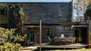 A modern wooden house with a patio area featuring outdoor furniture and a green door.