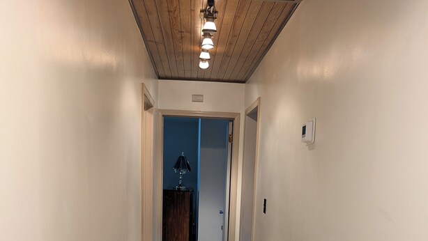 Un couloir étroit, doté d’un plancher en bois et de murs blancs, mène à une pièce dont la porte est bleue.