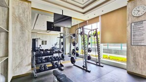 Ein Fitnessraum mit Gewichthebersportgeräten, einer Bank und einer Uhr an der Wand.