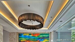 Eine moderne Lobby mit einem lebendigen abstrakten Wandgemälde, grünen Polstersitzmöglichkeiten und einer einzigartigen, runden Deckenleuchte.