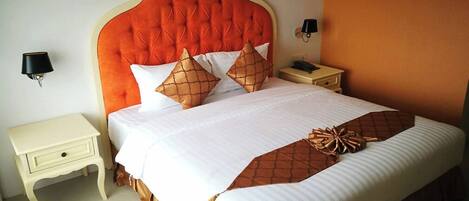Una cama bien hecha con un cabecero capitonado, ropa de cama blanca y almohadas decorativas. Hay mesitas de noche con lámparas y un aparador con un teléfono.