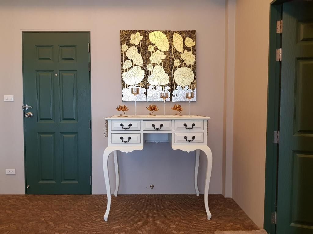 A room with a green door, a white dresser with drawers, and a decorative wall piece above it.