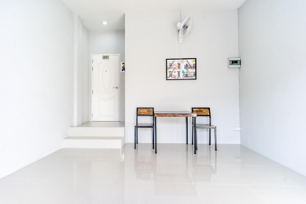 A clean, modern room with a white door, a small table with two chairs, and a wall-mounted fan.