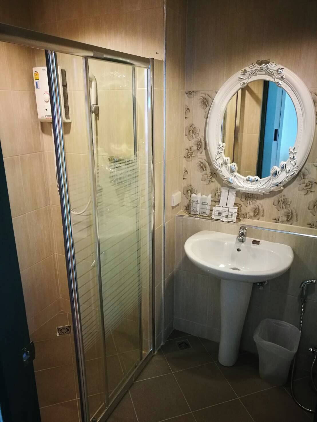 Un baño con ducha de vidrio, un lavamanos blanco con espejo y un cubo de basura.