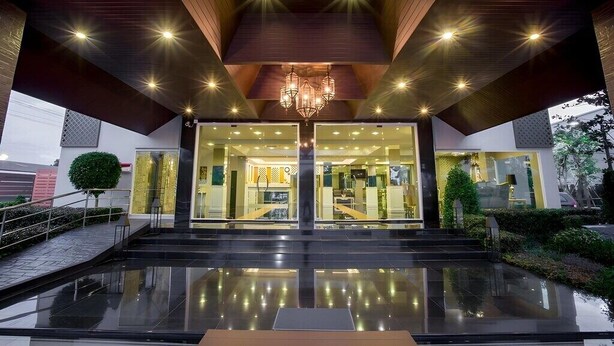 A modern hotel entrance with a reflective black floor, a central chandelier, and a glass facade.