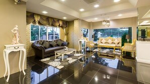 A spacious living room with a black tiled floor, a brown leather sofa, a white coffee table, and a gold armchair.