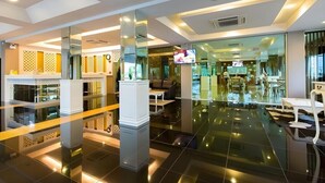 A modern hotel lobby with a glass partition, a seating area, and a television screen.