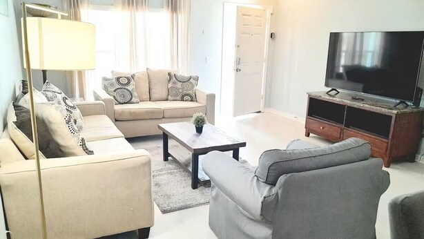 Ein Wohnzimmer mit Sofa, Sessel, Couchtisch, TV-Schrank und Vorhängen.