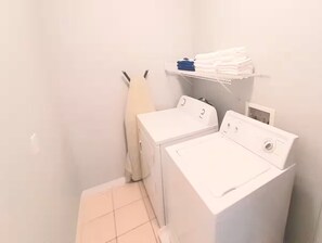 Un área de lavandería con dos lavadoras blancas y un estante con toallas dobladas.