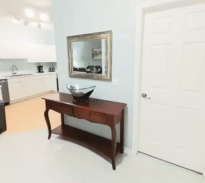 Una cocina moderna con armarios blancos, una mesa consola de madera, un cuenco de vidrio y un espejo enmarcados en la pared.
