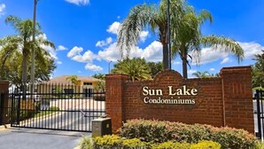 Eingezäunter Eingang zu den Sun Lake Condominiums, mit blauem Himmel und Palmen.