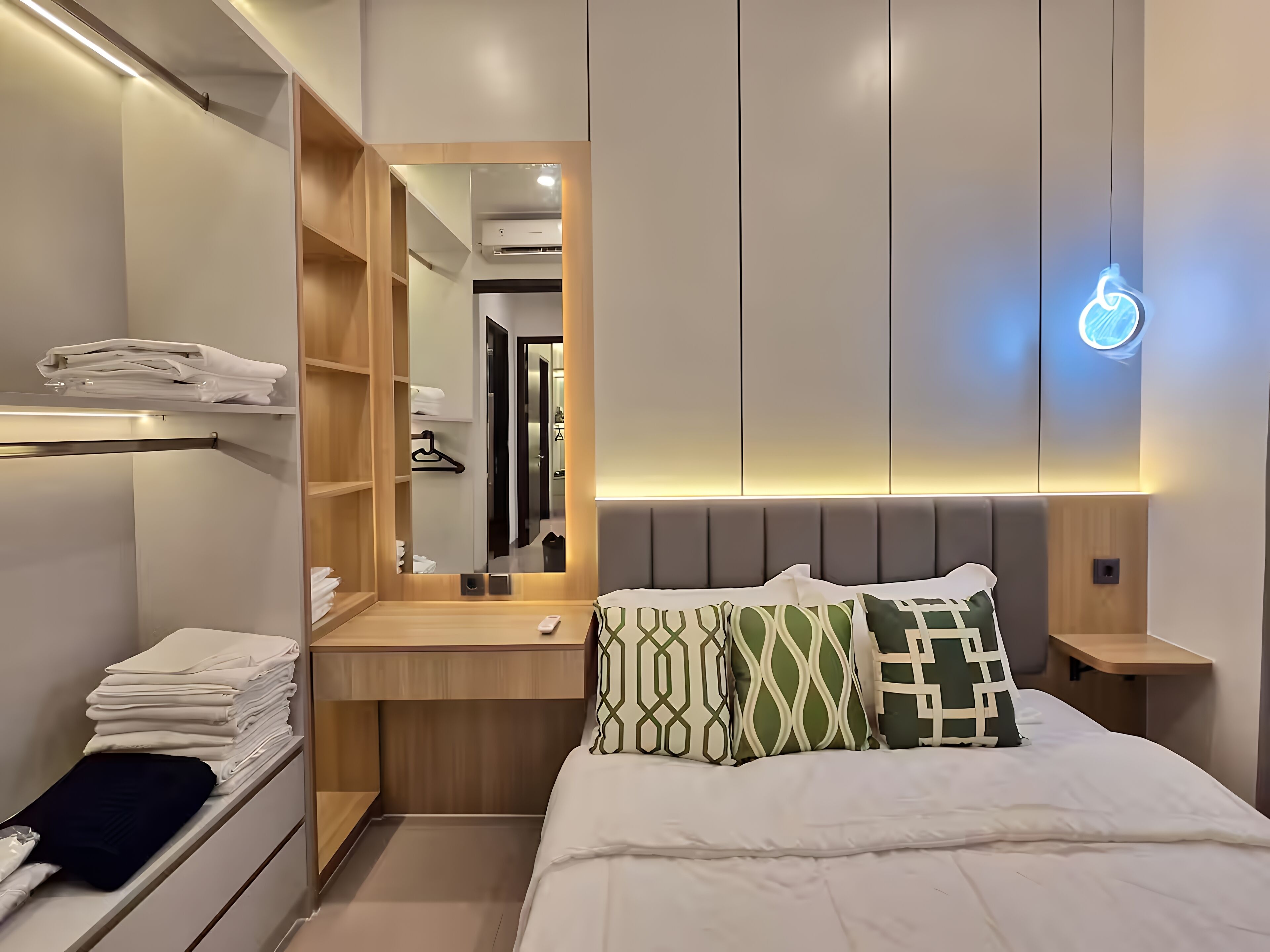 A modern hotel room with a neatly made bed, a built-in wardrobe, a bedside table, and a large mirror.