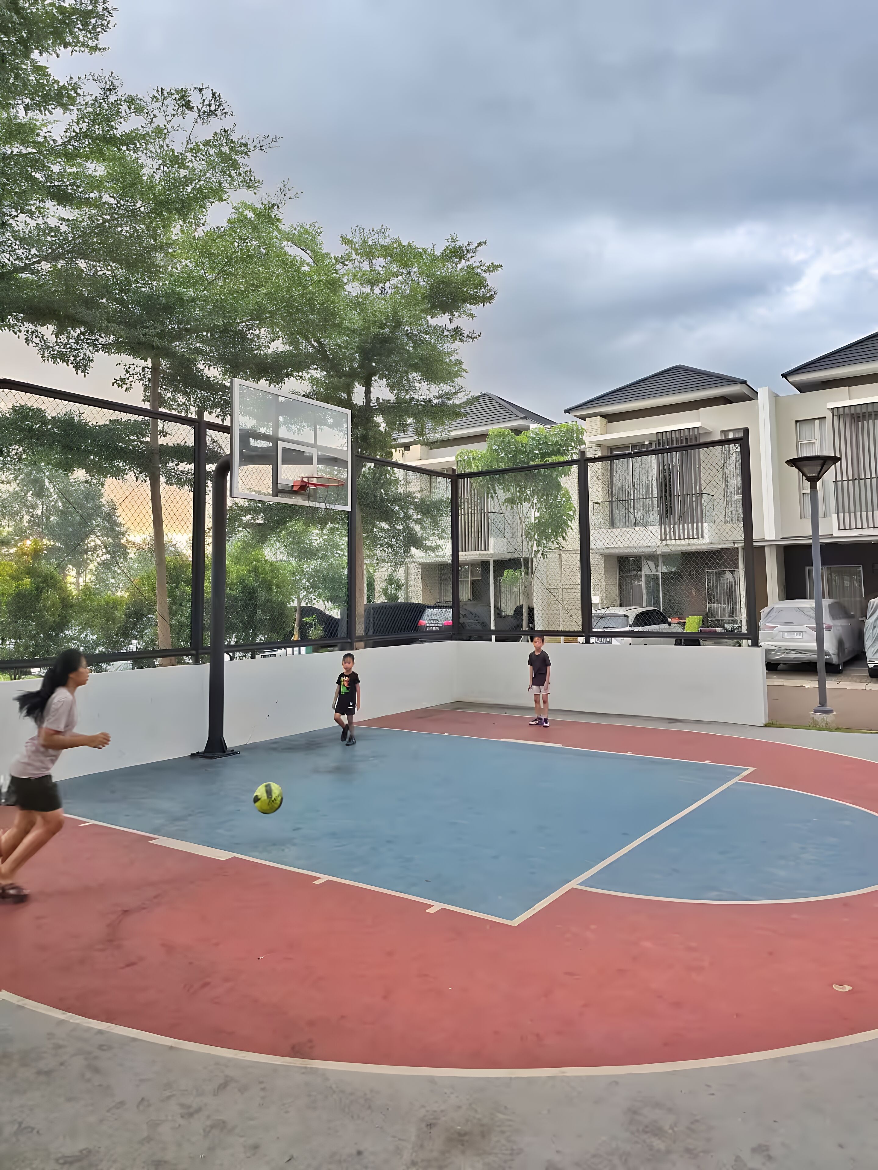 An outdoor basketball court with a net, surrounded by a fence and trees.