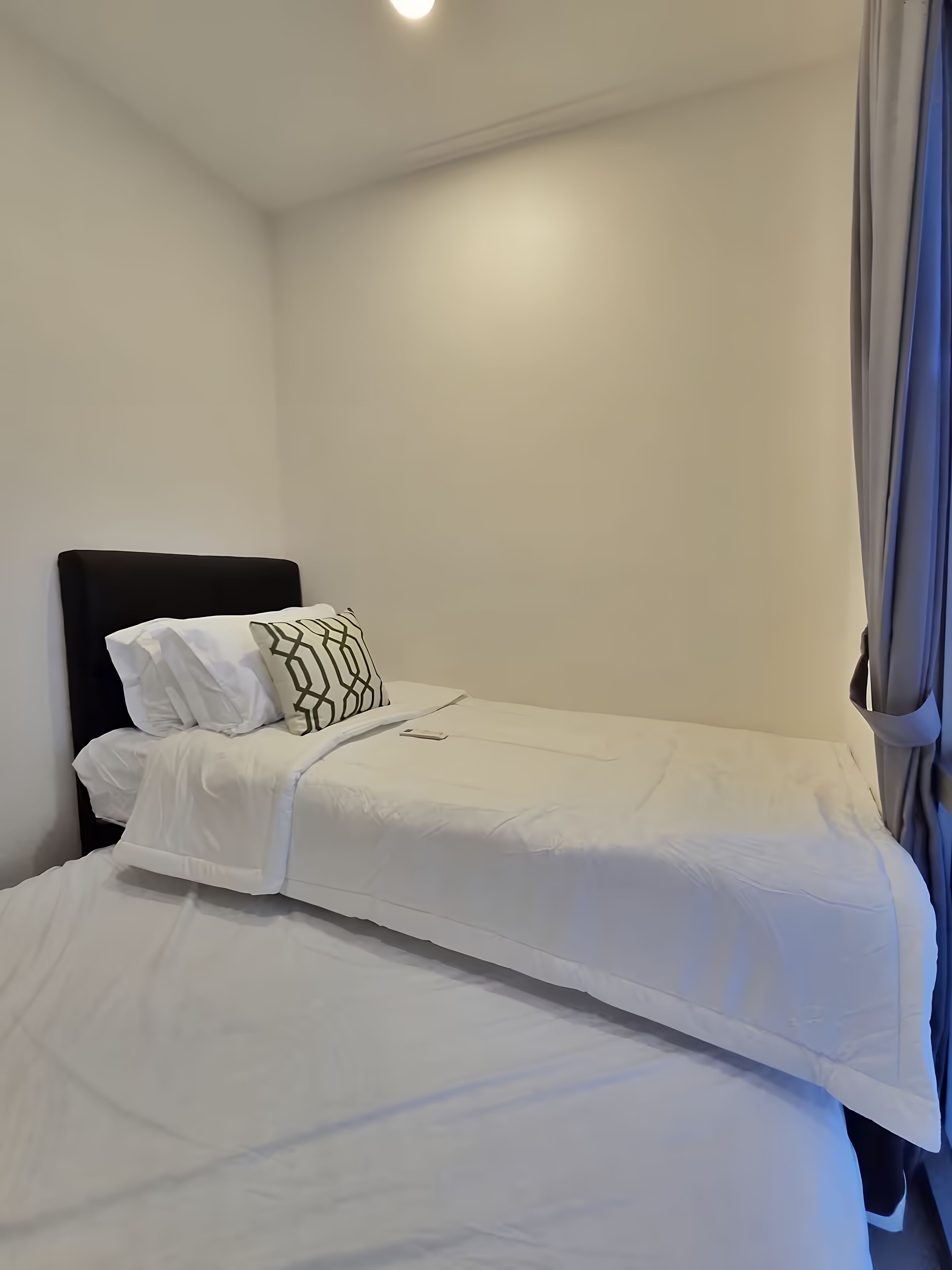 A single bed with white bedding and a black headboard in a room with plain white walls and a ceiling light.