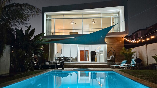 Une maison moderne dotée d’une piscine, d’un espace salon extérieur et de guirlandes lumineuses.