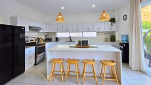 Une cuisine moderne avec des meubles blancs, un réfrigérateur noir, un îlot central doté de tabourets et un éclairage suspendu.