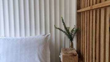 A bedroom with a bed, white curtains, a wooden headboard, and a small plant on a wooden nightstand.