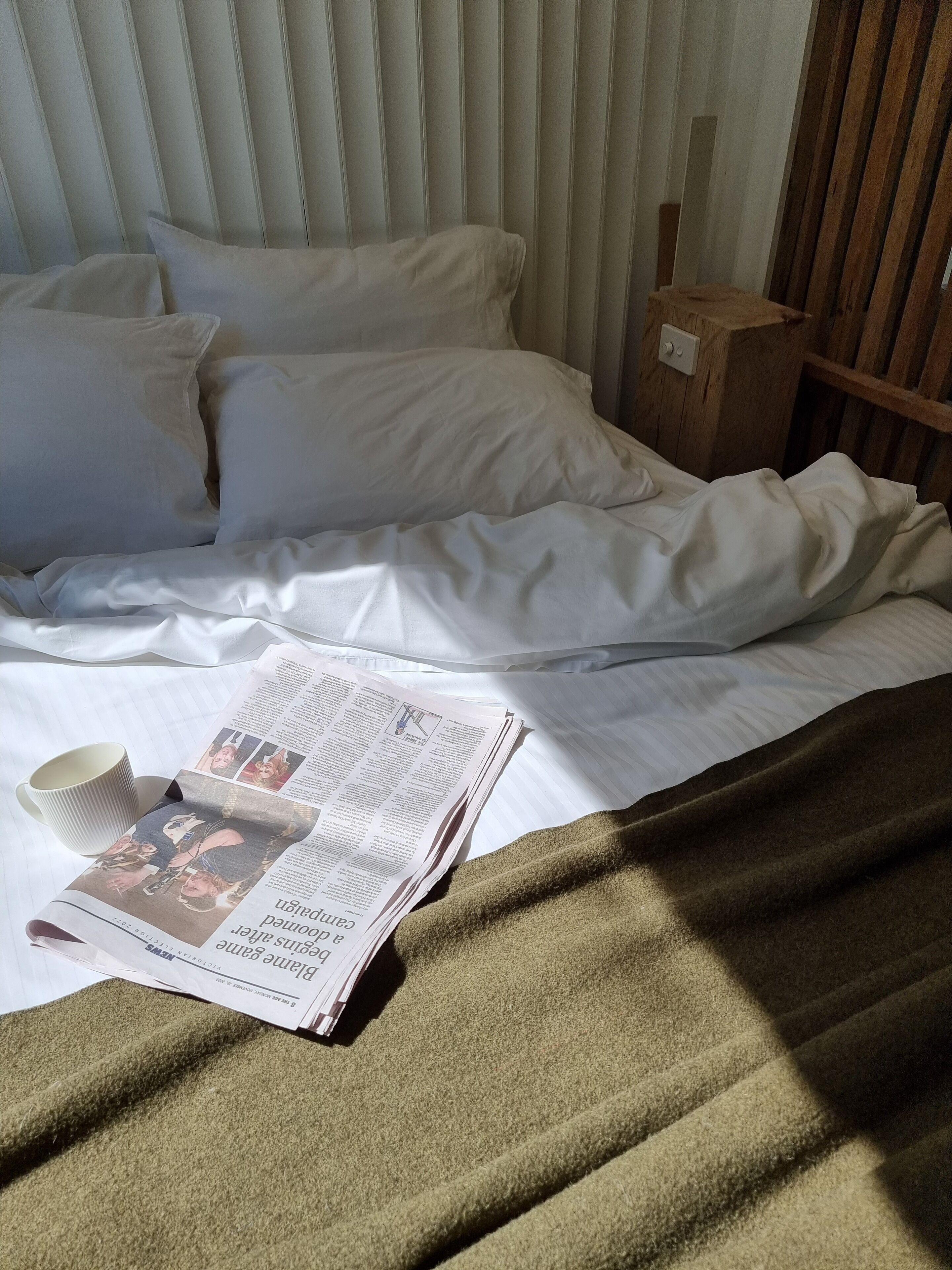 Una cama bien hecha con sábanas blancas, una manta verde y un periódico sobre la cama.