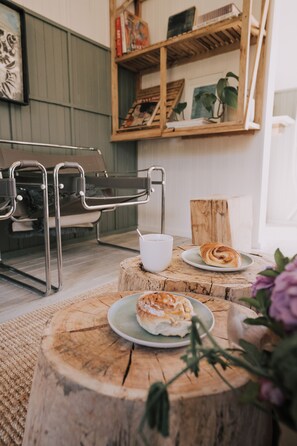 Una habitación acogedora con un banco de madera, una pequeña mesa con un croissant y una estantería con libros y plantas.