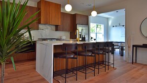 Una cocina moderna con armarios de madera, una isla central con taburetes altos e iluminación colgante.