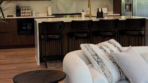 Una cocina moderna con armarios de madera, una isla central con taburetes y una zona de comedor con sofá y una pequeña mesa redonda.