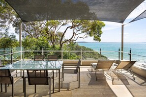 An outdoor seating area with a glass table and chairs, overlooking a body of water.