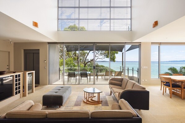 A spacious living area with a large sofa, a coffee table, and a view of the sea through floor-to-ceiling windows.