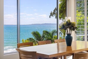 Zona pranzo con vista sul mare, un tavolo, sedie e un vaso con fiori.