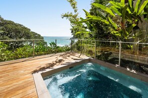 A wooden deck with a hot tub and a glass railing overlooking a body of water.