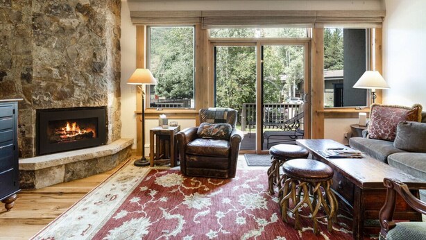 A cozy living room with a stone fireplace, a leather armchair, a sofa, and a dining table. - West Vail Ptarmigan Townhome - Steps to Bus (Vail)