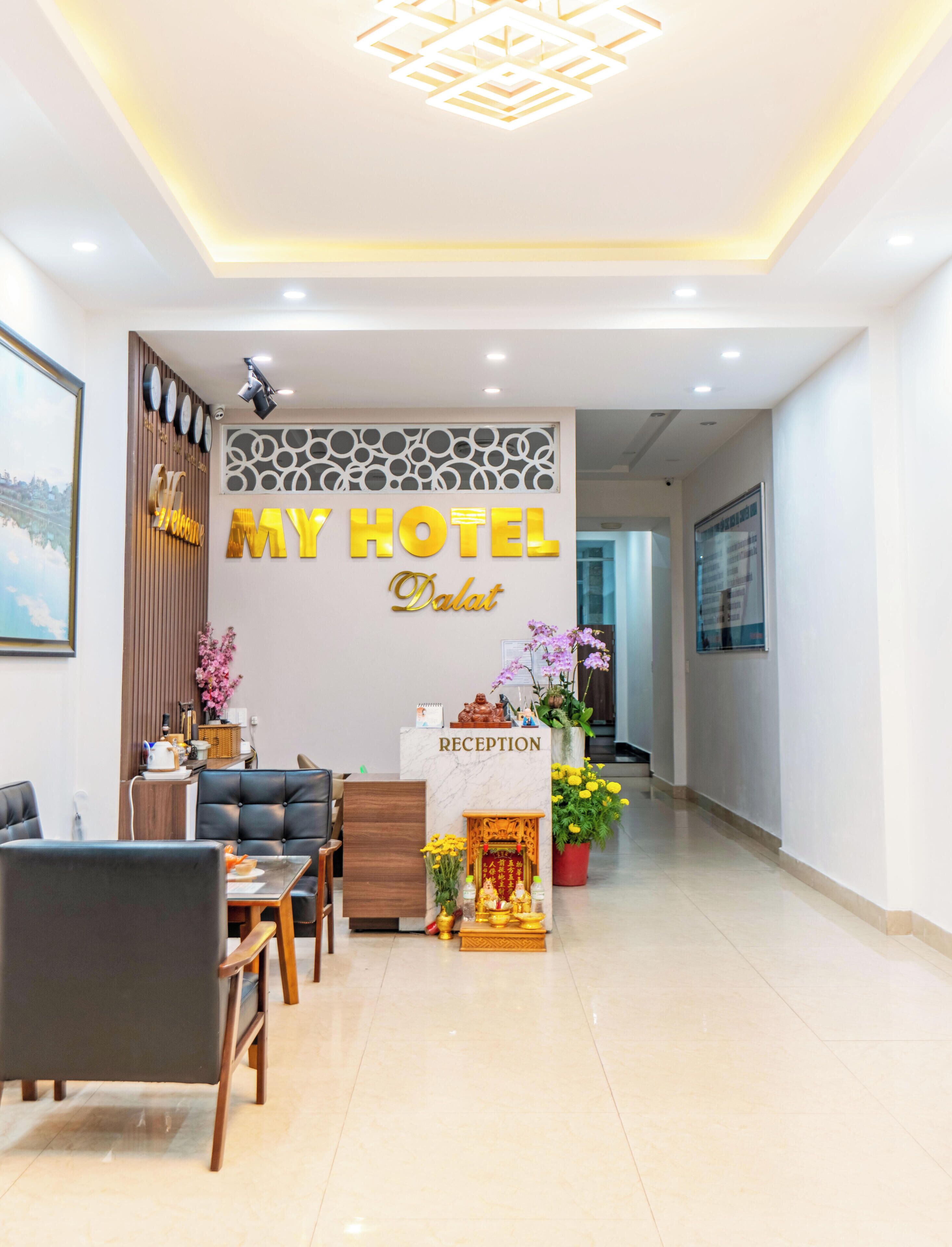 A hotel reception area with a reception desk, seating, and a decorative wall.