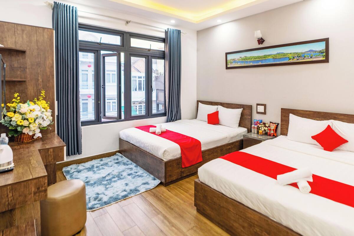 A hotel room with two beds, a desk, a TV, and a window with curtains.