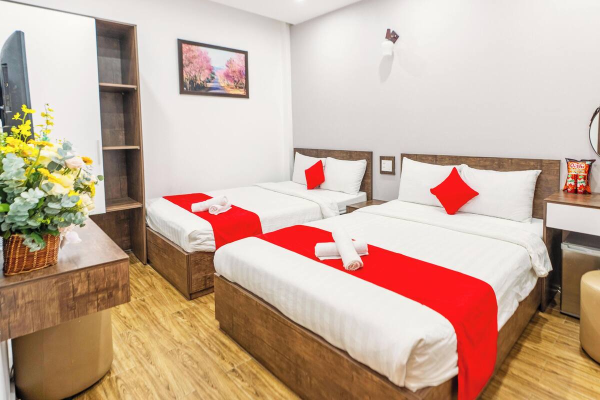 A hotel room with two beds, a desk, a mirror, and a small stool.