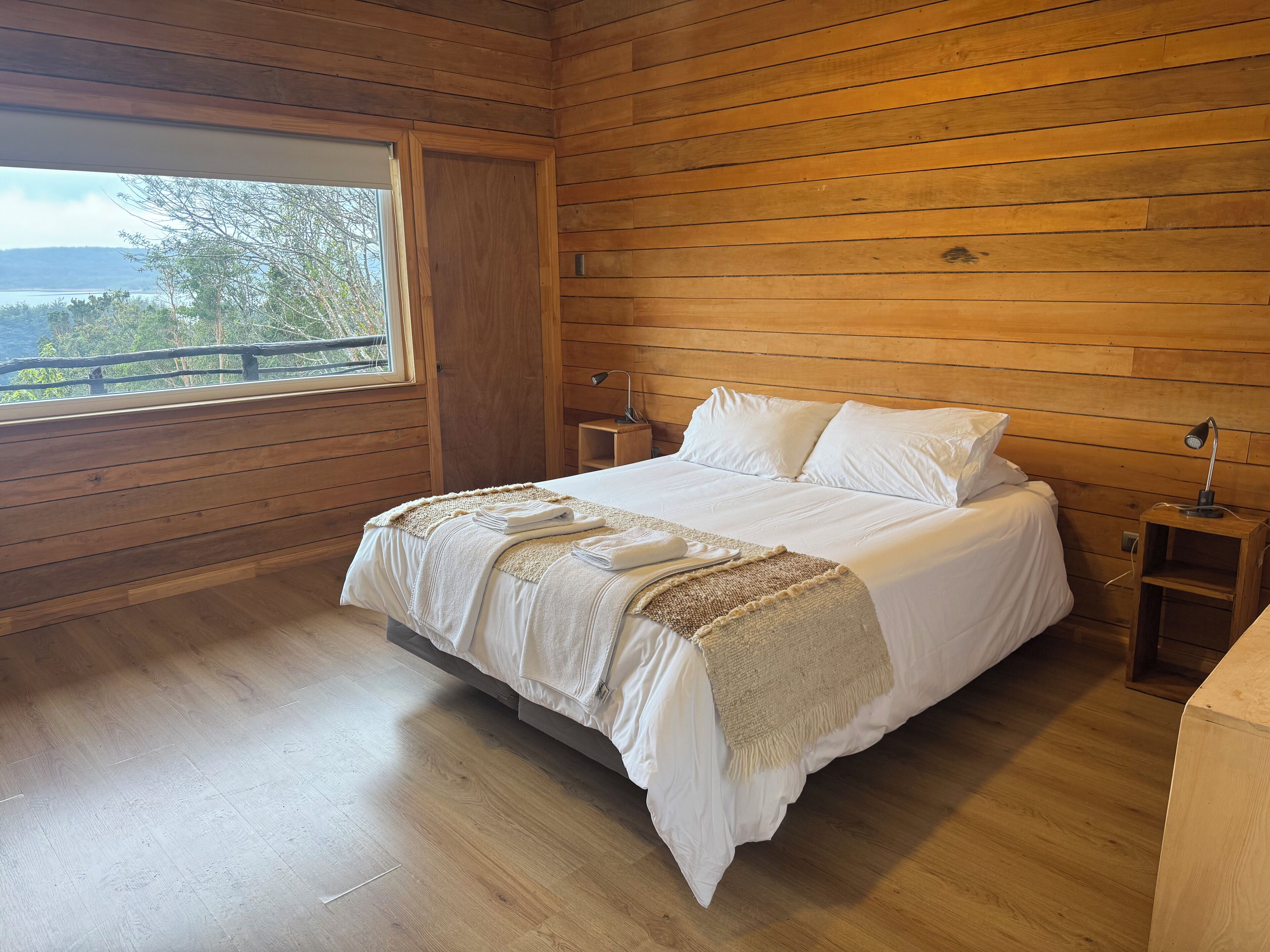 Una habitación con paneles de madera, una cama, un ventanal y una mesita de noche.