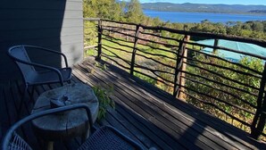 A wooden deck with two wicker chairs and a small round table, overlooking a lake with a distant shoreline. - Huillín Lodge (Chonchi)
