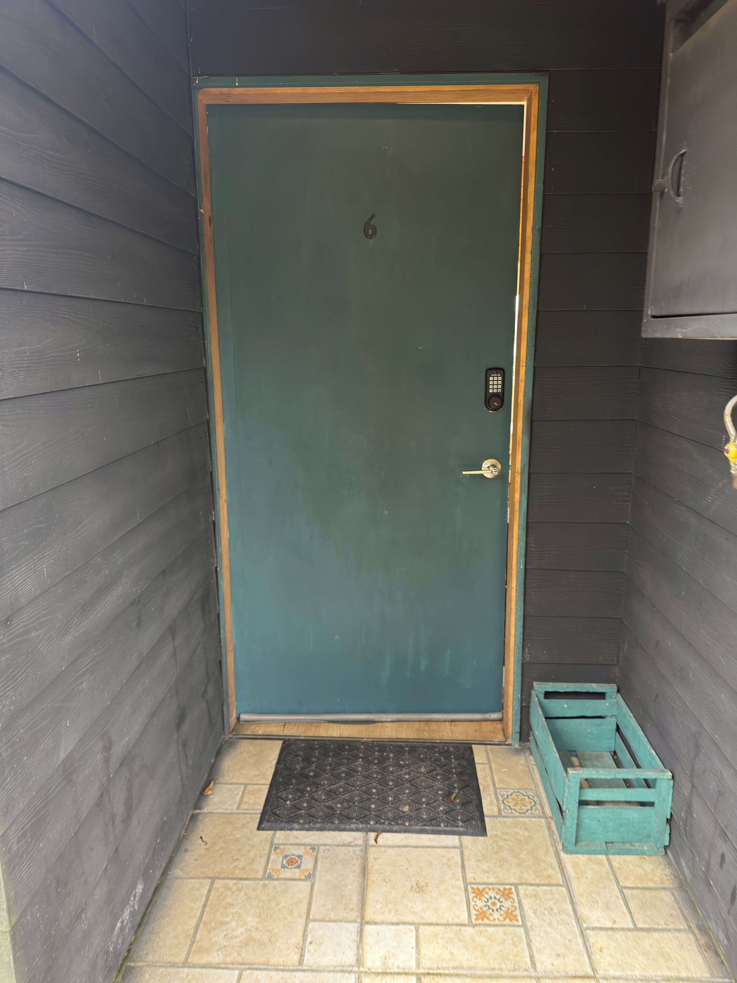 Un cuarto pequeño y cerrado con una puerta verde, un teclado de bloqueo y un pequeño cofre de madera.