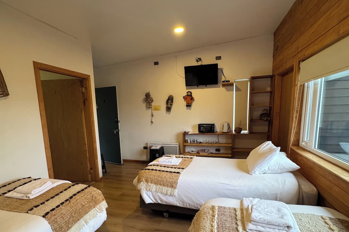 A hotel room with two beds, a TV mounted on the wall, a wooden wardrobe, and a window with blinds.