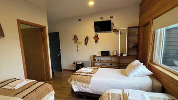 A hotel room with two beds, a TV mounted on the wall, a wooden wardrobe, and a window with blinds.