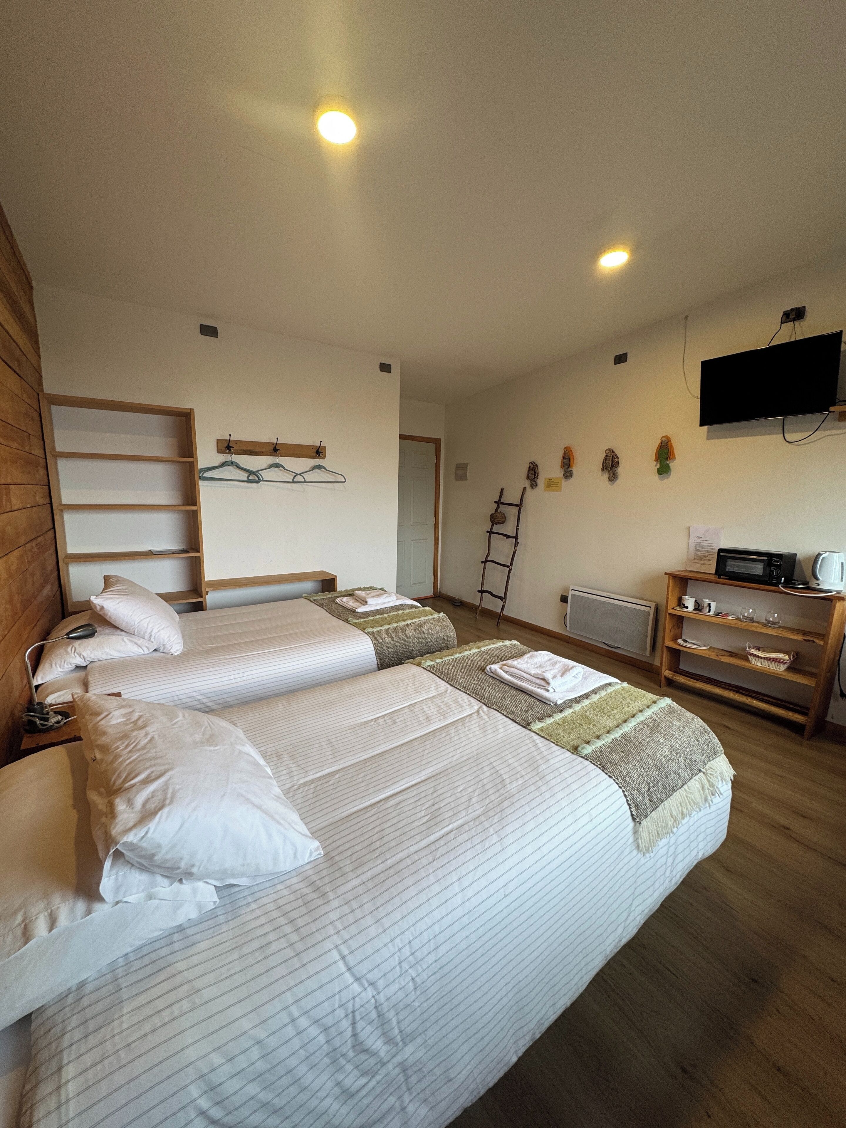 A hotel room with two beds, a TV, a wooden dresser, and a ladder.