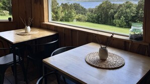 A wooden interior with a large window offering a view of a lake and hills. Tables with woven placemats and vases are visible. - Huillín Lodge (Chonchi)