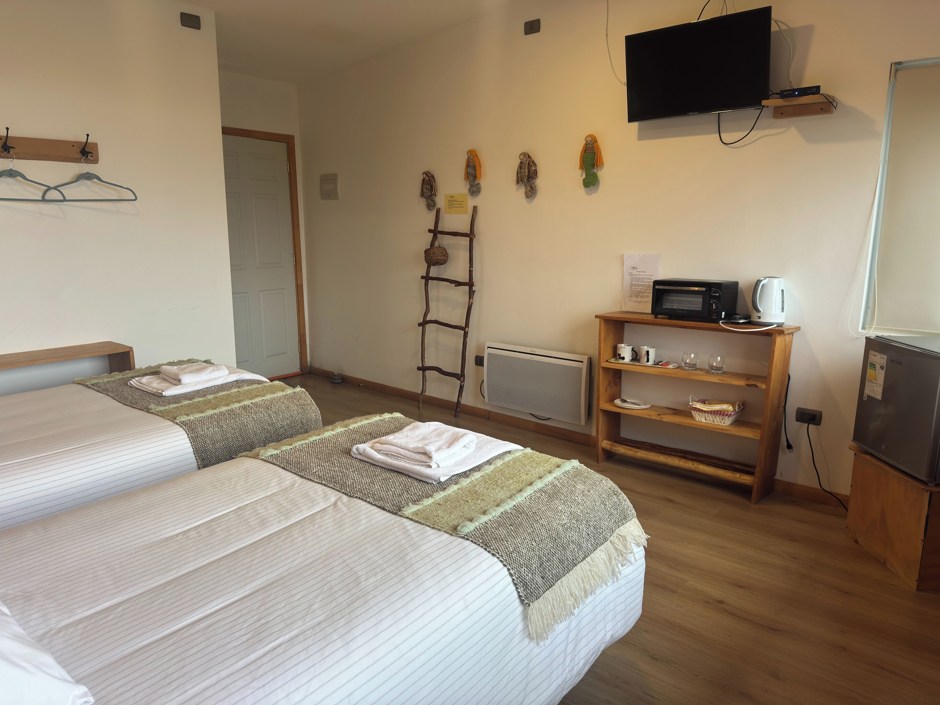 A hotel room with two beds, a TV, a microwave, a refrigerator, a shelf with mugs and glasses, and a ladder against the wall.