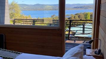 A bedroom with a large window offering a view of a lake and hills.