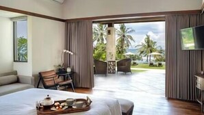 Quarto de hotel com cama, mesa de jantar com café da manhã, televisão e vista para palmeiras e piscina.