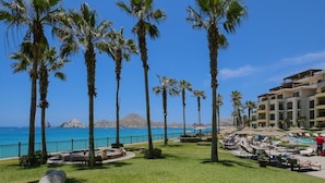 A resort with palm trees, a pool, and a view of the ocean. - 3 BR Panoramic OF villa that sleeps 10 people, just steps from the beach and pool! (Cabo San Lucas)