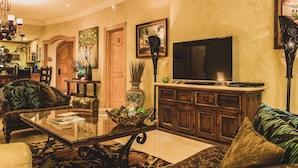 A spacious living room with a large flat-screen TV, wooden furniture, and a chandelier. - 3 BR Panoramic OF villa that sleeps 10 people, just steps from the beach and pool! (Cabo San Lucas)