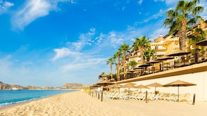 A beach resort with sun loungers, umbrellas, and palm trees. - 3 BR Panoramic OF villa that sleeps 10 people, just steps from the beach and pool! (Cabo San Lucas)
