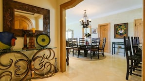 A dining area with a round table and chairs, a chandelier, and a mirror with decorative elements. - 3 BR Panoramic OF villa that sleeps 10 people, just steps from the beach and pool! (Cabo San Lucas)
