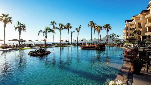 A clear blue pool with lounge chairs and palm trees, surrounded by a resort building. - Newly Renovated Luxury Villa! Medano Beachfront! Overlooking Pools, and Sea of Cortez! (Cabo San Lucas)