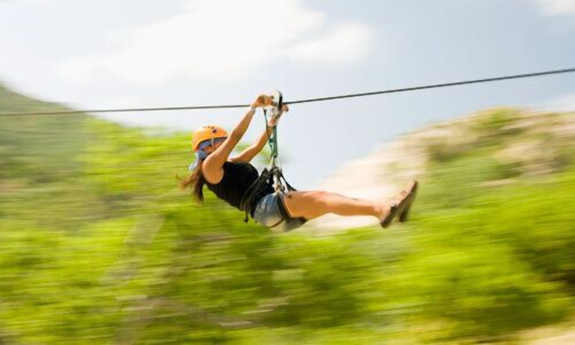 A person ziplining with a harness and helmet, suspended on a cable.