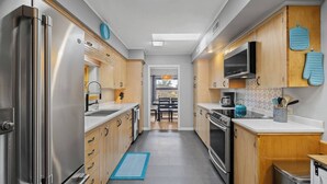 Une cuisine moderne dotée d’appareils électroménagers en acier inoxydable, de meubles de rangement en bois et d’un tapis bleu sur le sol.